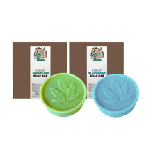 Load image into Gallery viewer, Two round soap bars from Green Apron are pictured in front of their respective brown packages. One soap bar is green, labeled &quot;Lady Green Hemp Soap Bar,&quot; and the other is blue, also labeled &quot;Lady Green Hemp Soap Bar.&quot; Both soaps feature a leaf imprint on top.
